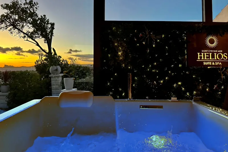 Bain balnéo privatif de la suite Orion à Saint-Cyr-sur-Mer, avec éclairage bleu et vue sur le coucher du soleil.