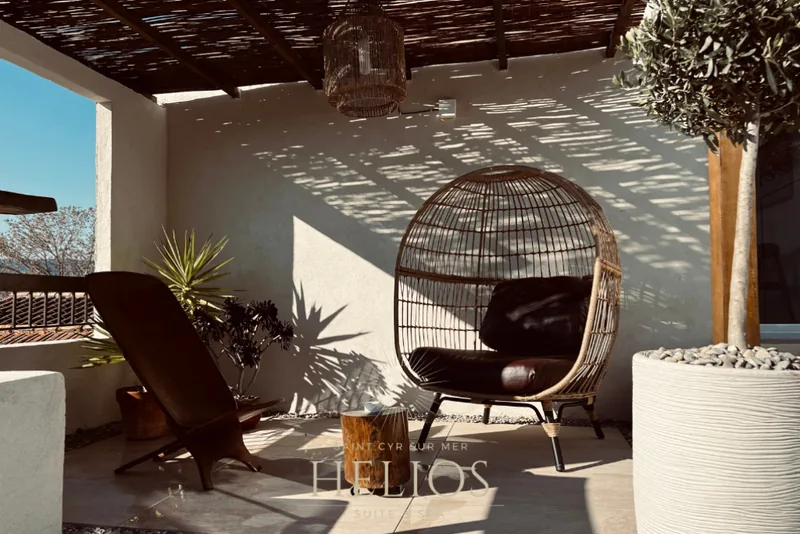Terrasse privative d’Helios, avec fauteuil suspendu et salon extérieur sous la pergola.